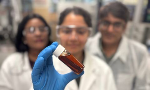 Two women and one man in a lab - the middle person is holding a vile of brown liquid..